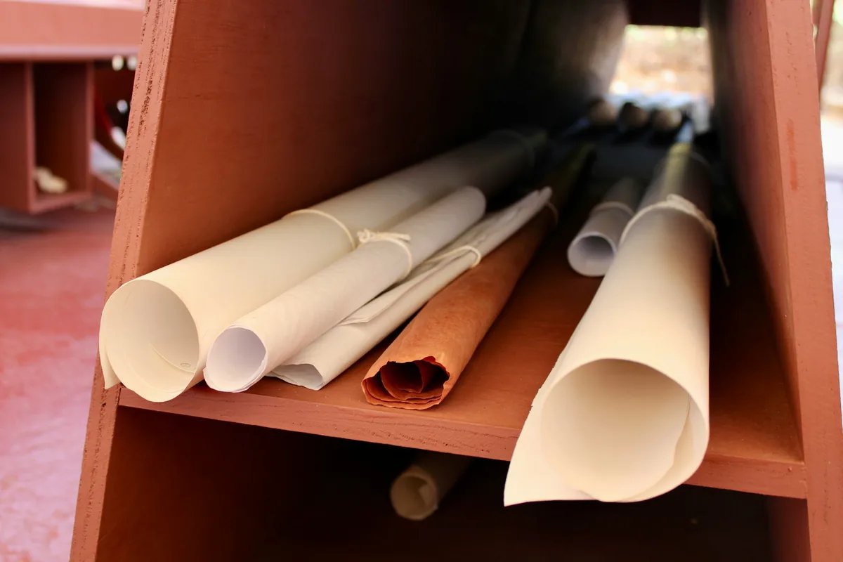 Several rolled drawing sheets tied with string, stored on a wooden shelf.