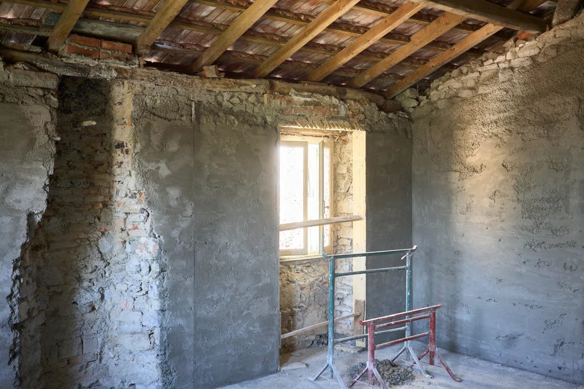 An empty room under renovation, with a ladder standing in front of a window and bare walls.