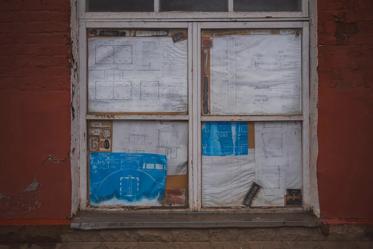 Technical drawings and blueprints taped up inside an old window set in a red brick wall.